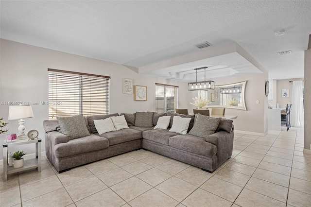 tiled living room featuring a tray ceiling, a textured ceiling, a chandelier, and plenty of natural light