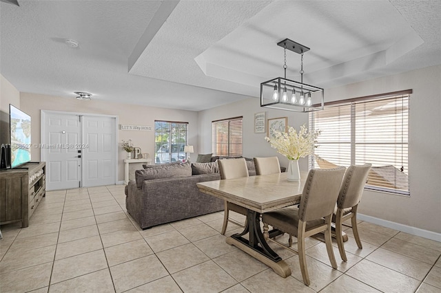 tiled dining space with a textured ceiling, a raised ceiling, a notable chandelier, and a wealth of natural light