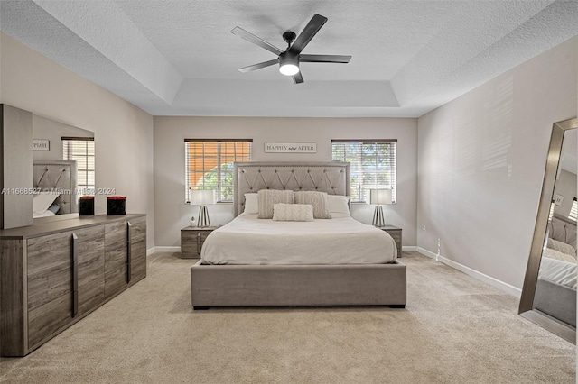 bedroom with multiple windows, a raised ceiling, ceiling fan, and light colored carpet