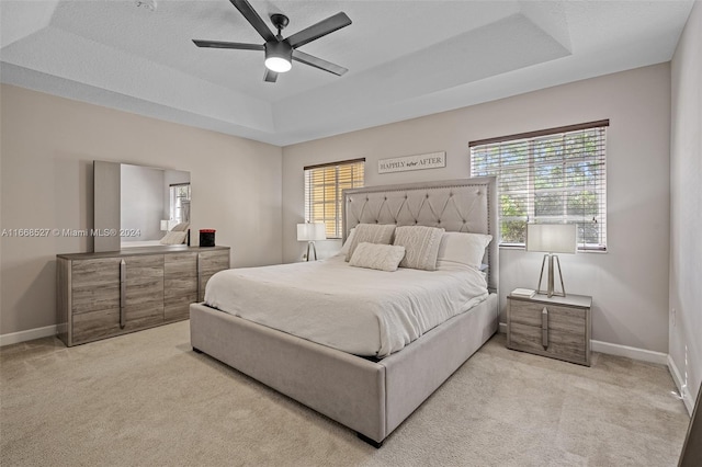 carpeted bedroom featuring multiple windows, a tray ceiling, and ceiling fan