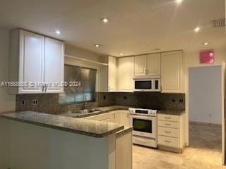 kitchen with decorative backsplash, kitchen peninsula, white cabinetry, and white appliances