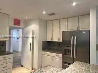 kitchen featuring light stone countertops, stainless steel fridge, white cabinets, and decorative backsplash