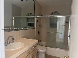 full bathroom with vanity, toilet, combined bath / shower with glass door, and decorative backsplash