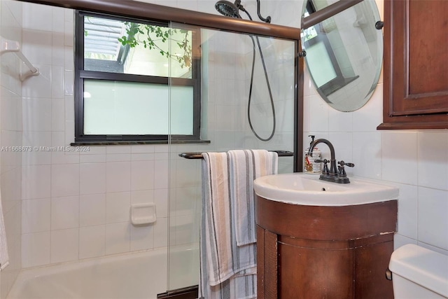 bathroom with tile walls, a shower with door, vanity, and toilet