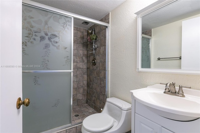 bathroom with a textured ceiling, a shower with shower door, vanity, and toilet