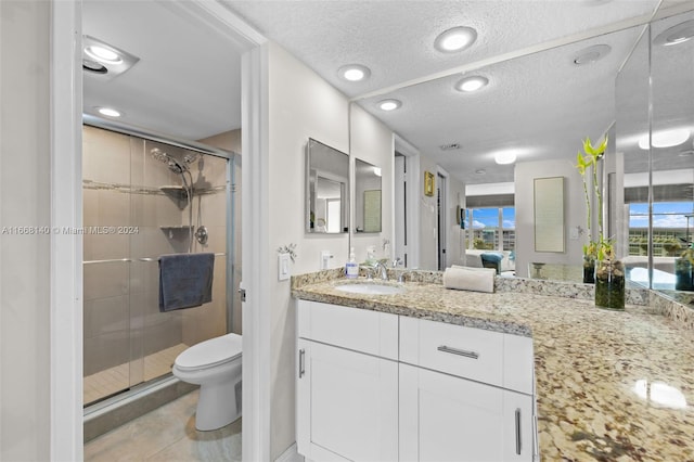 bathroom with vanity, a textured ceiling, tile patterned floors, toilet, and a shower with door