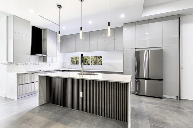 kitchen featuring hanging light fixtures, a kitchen island with sink, stainless steel refrigerator, wall chimney exhaust hood, and sink