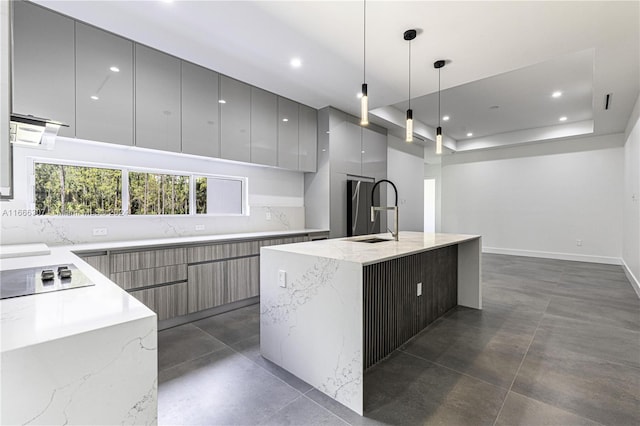 kitchen featuring pendant lighting, light stone counters, an island with sink, and black electric cooktop