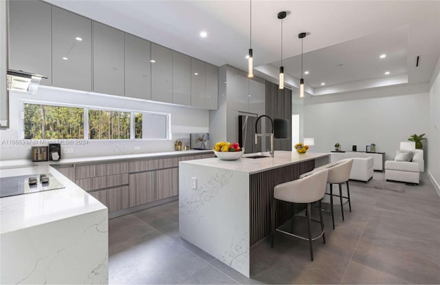 kitchen featuring black electric cooktop, light stone countertops, hanging light fixtures, and an island with sink