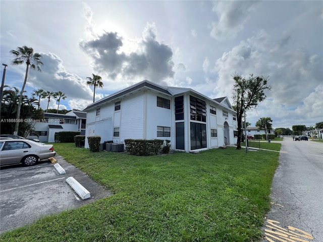 view of property exterior featuring central air condition unit, uncovered parking, and a lawn