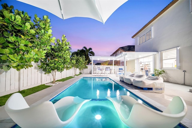 pool at dusk with a pool with connected hot tub, a fenced backyard, and a patio