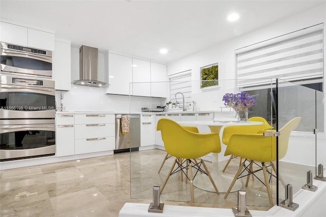 kitchen featuring stainless steel appliances, light countertops, wall chimney exhaust hood, and modern cabinets