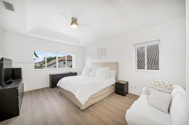 bedroom featuring light wood-style flooring, a raised ceiling, visible vents, and baseboards