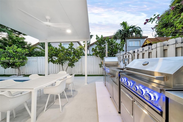 view of patio / terrace with exterior kitchen, outdoor dining area, a fenced backyard, and a ceiling fan