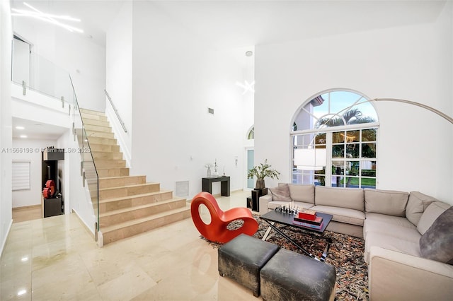 living area featuring visible vents, marble finish floor, stairway, and a towering ceiling