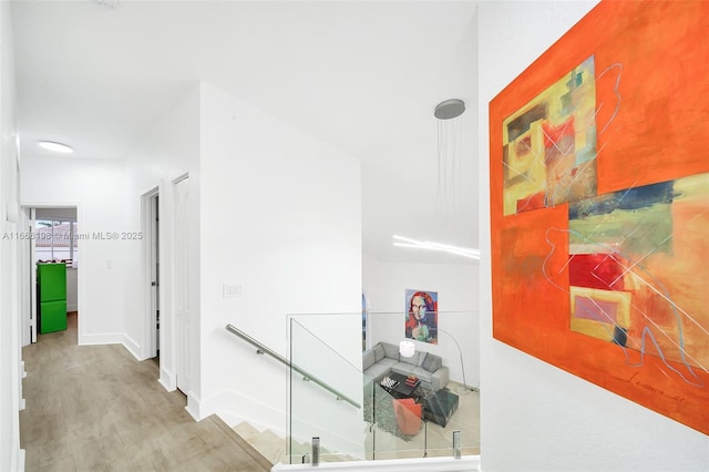 corridor featuring light wood-style flooring, baseboards, and an upstairs landing