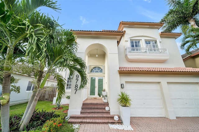 mediterranean / spanish-style home with a balcony, an attached garage, fence, decorative driveway, and stucco siding