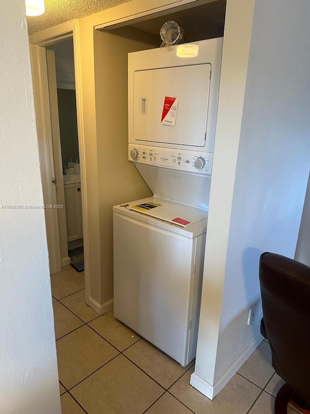 laundry area featuring light tile patterned floors, baseboards, and stacked washing maching and dryer