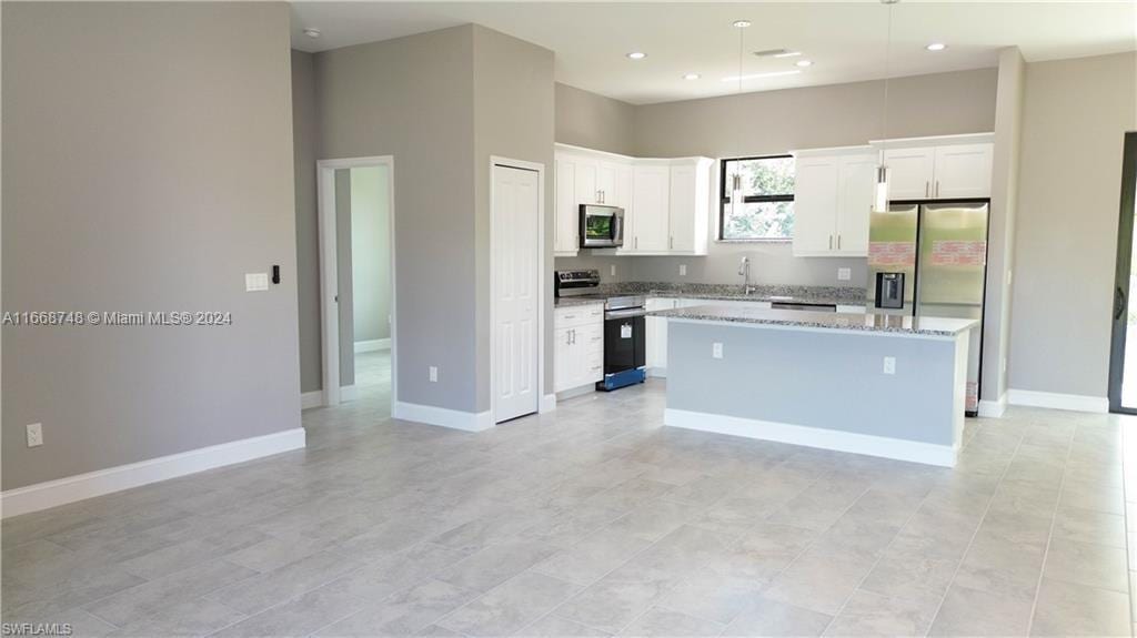 kitchen featuring light stone countertops, stainless steel appliances, white cabinetry, and a center island