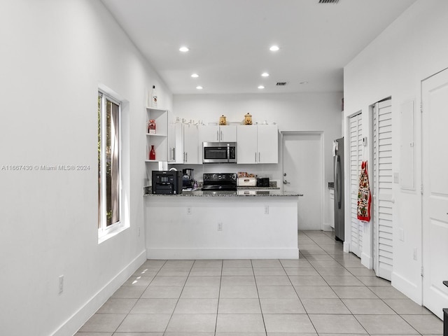 kitchen with light tile patterned floors, kitchen peninsula, white cabinetry, stainless steel appliances, and dark stone counters