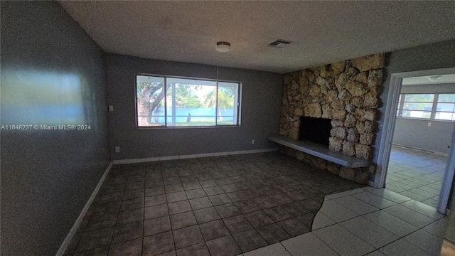 unfurnished living room with a stone fireplace and tile patterned flooring