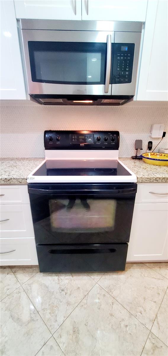 interior details with light stone counters, black / electric stove, and white cabinetry