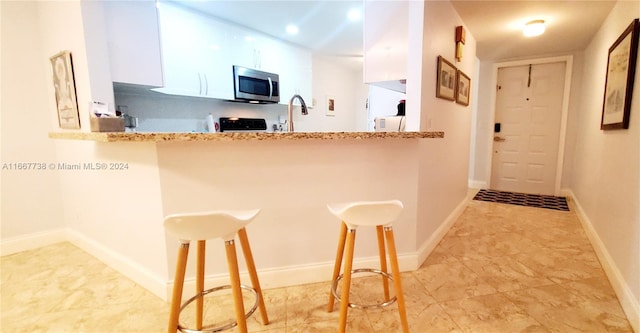 kitchen with sink, white cabinetry, kitchen peninsula, a kitchen breakfast bar, and light stone countertops