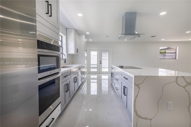 kitchen featuring appliances with stainless steel finishes, light stone counters, white cabinets, sink, and wall chimney range hood