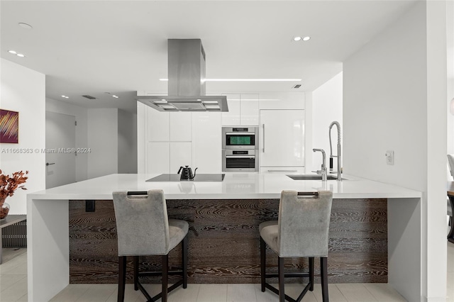 kitchen featuring sink, a breakfast bar area, white cabinets, island exhaust hood, and kitchen peninsula