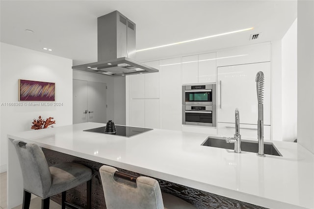 kitchen with white cabinets, island exhaust hood, a kitchen bar, black electric stovetop, and double oven