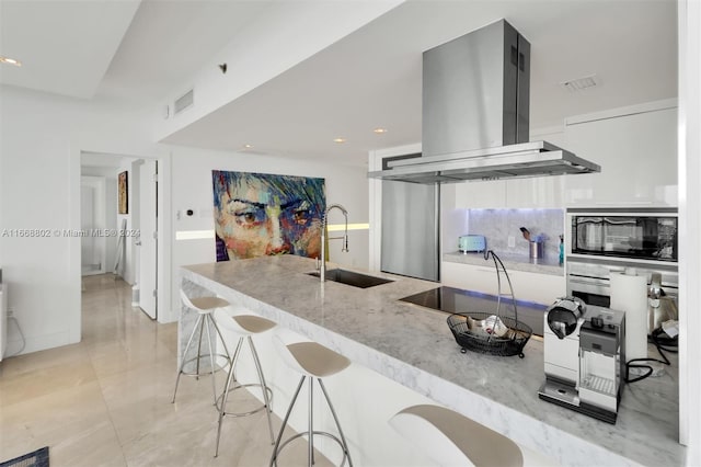 kitchen with island range hood, light stone countertops, black appliances, a kitchen bar, and sink