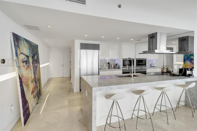 kitchen featuring white cabinetry, a breakfast bar area, stainless steel oven, sink, and wall chimney range hood