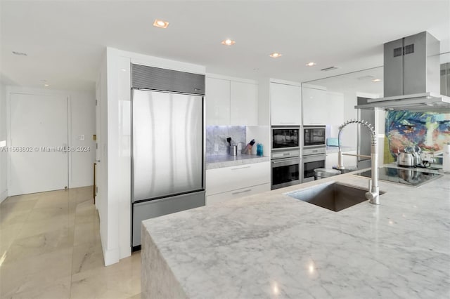 kitchen with white cabinets, light stone counters, island range hood, and appliances with stainless steel finishes