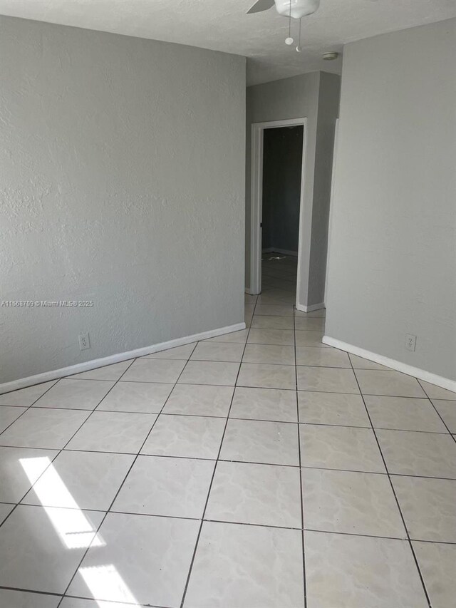 spare room with light tile patterned floors, a ceiling fan, and baseboards