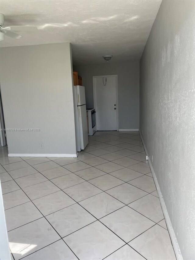 hallway with light tile patterned floors, a textured wall, and baseboards