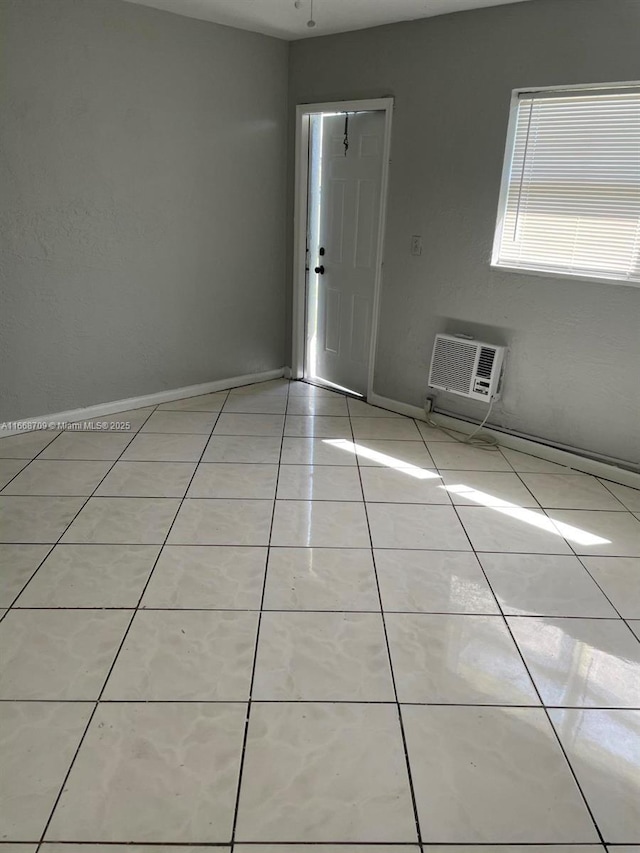 empty room with baseboards, an AC wall unit, and light tile patterned flooring