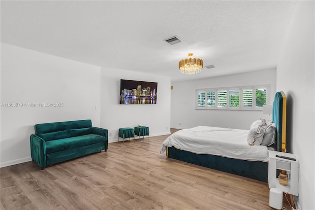 bedroom featuring hardwood / wood-style floors, a textured ceiling, and an inviting chandelier