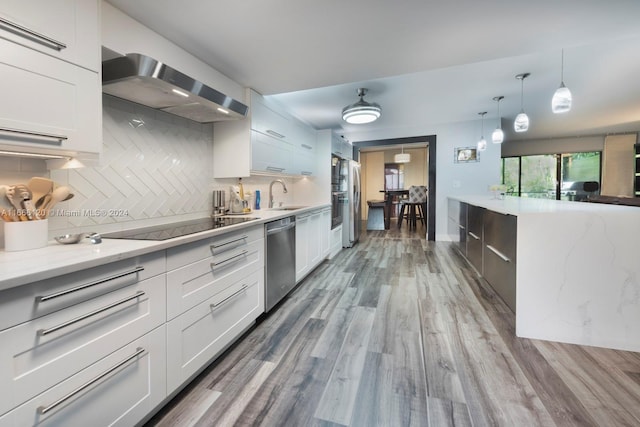 kitchen featuring white cabinets, backsplash, stainless steel appliances, hardwood / wood-style flooring, and wall chimney range hood