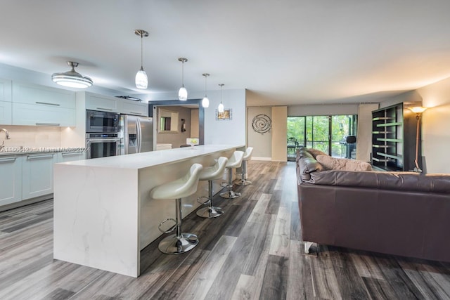 kitchen featuring pendant lighting, white cabinetry, a kitchen breakfast bar, stainless steel appliances, and hardwood / wood-style floors