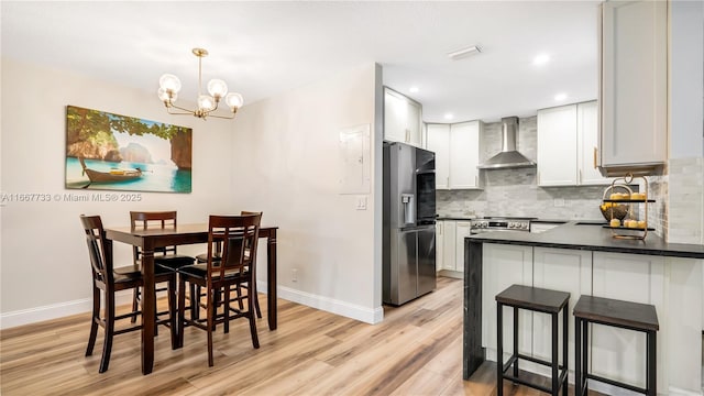 kitchen featuring white cabinetry, decorative light fixtures, appliances with stainless steel finishes, wall chimney range hood, and backsplash