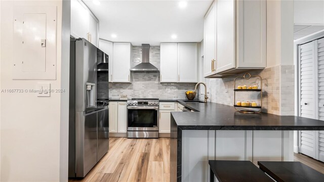 kitchen with sink, wall chimney range hood, kitchen peninsula, a breakfast bar, and appliances with stainless steel finishes