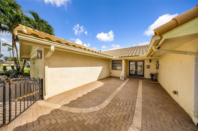 doorway to property with a patio, fence, stucco siding, french doors, and a tiled roof