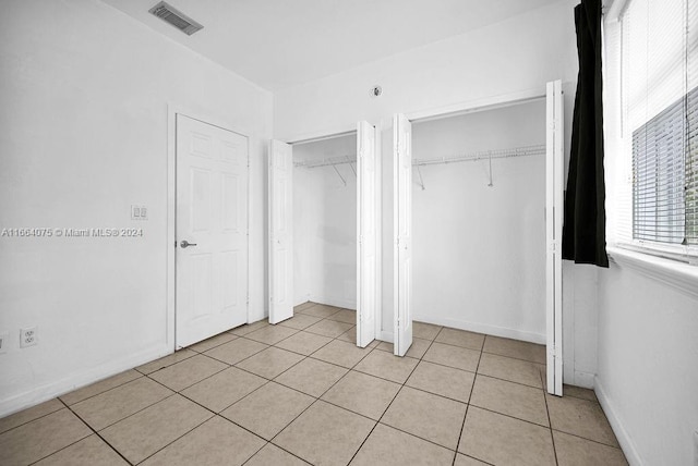 unfurnished bedroom with two closets and light tile patterned floors