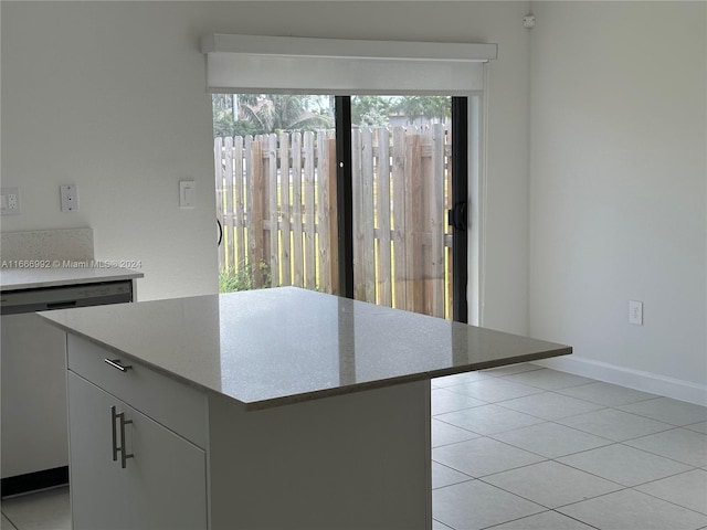 kitchen with light tile patterned flooring, stainless steel dishwasher, white cabinetry, a center island, and light stone countertops