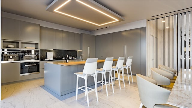 kitchen with gray cabinetry, a kitchen bar, oven, and decorative backsplash