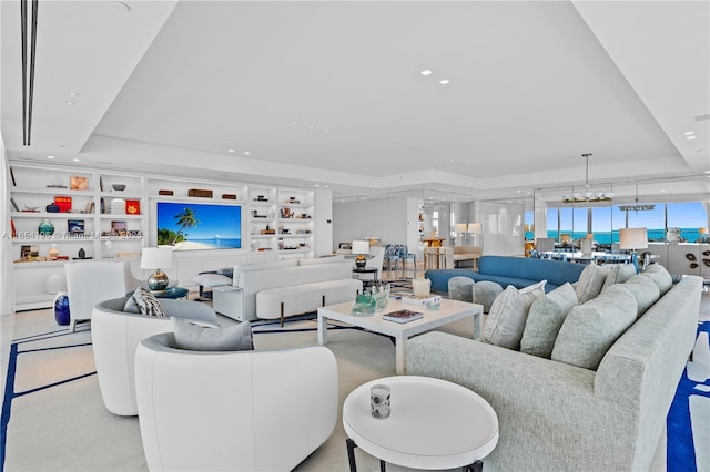 living room featuring a raised ceiling, a chandelier, and built in shelves