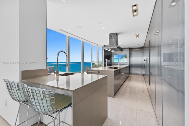 kitchen with wall chimney exhaust hood, modern cabinets, a sink, a water view, and marble finish floor