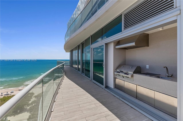 balcony with sink, a water view, a grill, a beach view, and an outdoor kitchen