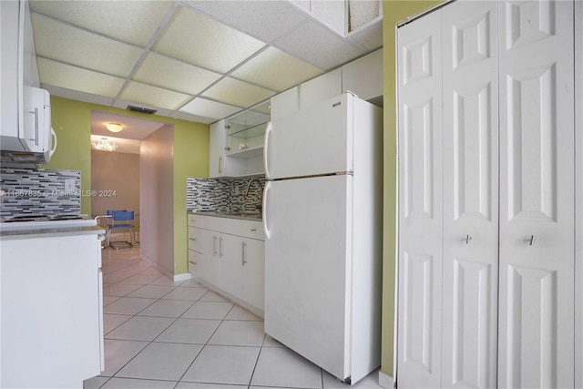 kitchen with light tile patterned floors, backsplash, white cabinetry, a drop ceiling, and white appliances