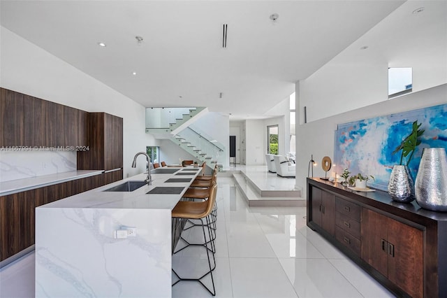 kitchen with a breakfast bar, light stone countertops, light tile patterned floors, sink, and a spacious island